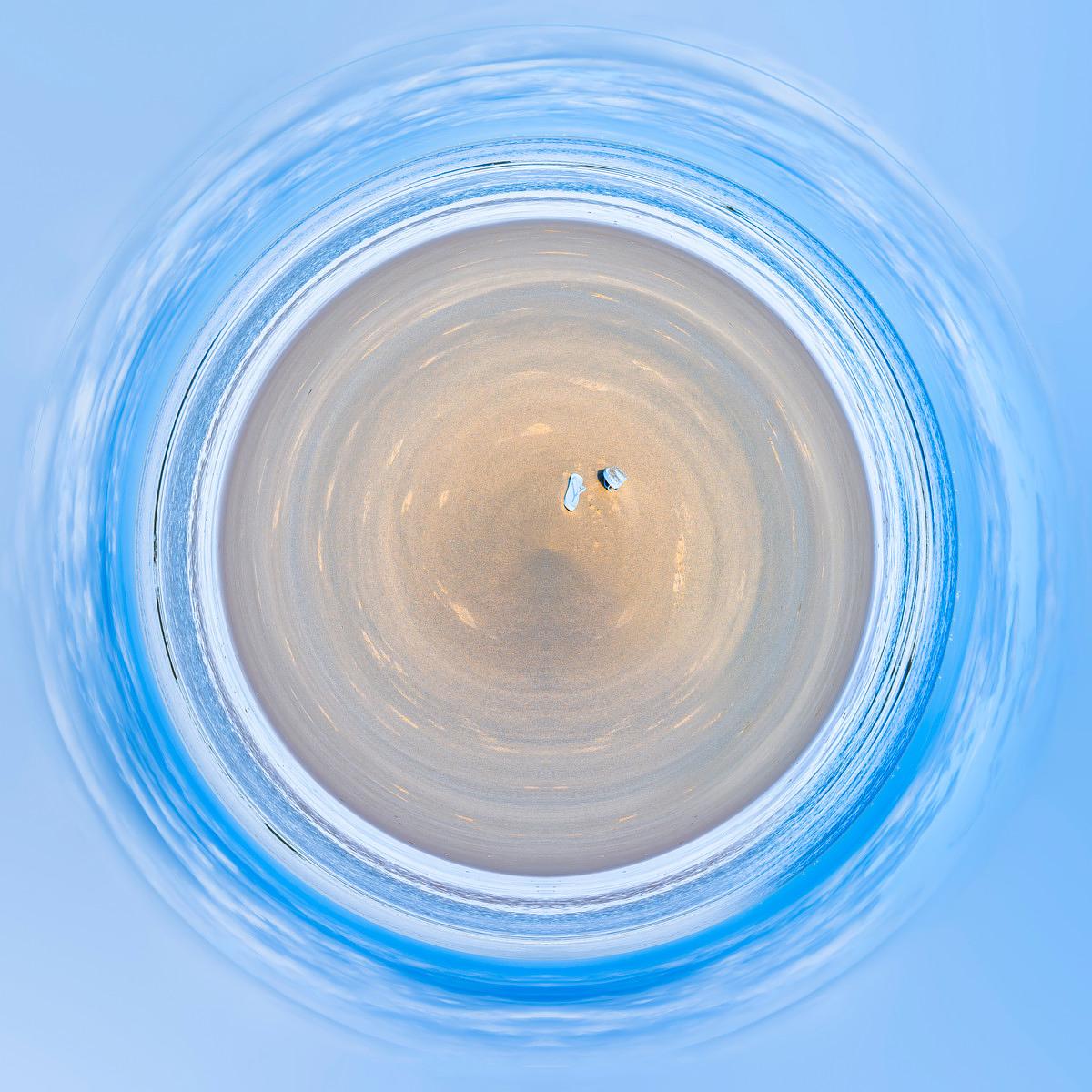 Céleste cercle de ciel bleu entourant une plage vue en rotation, formant des spirales où les vagues viennent lécher le sable.