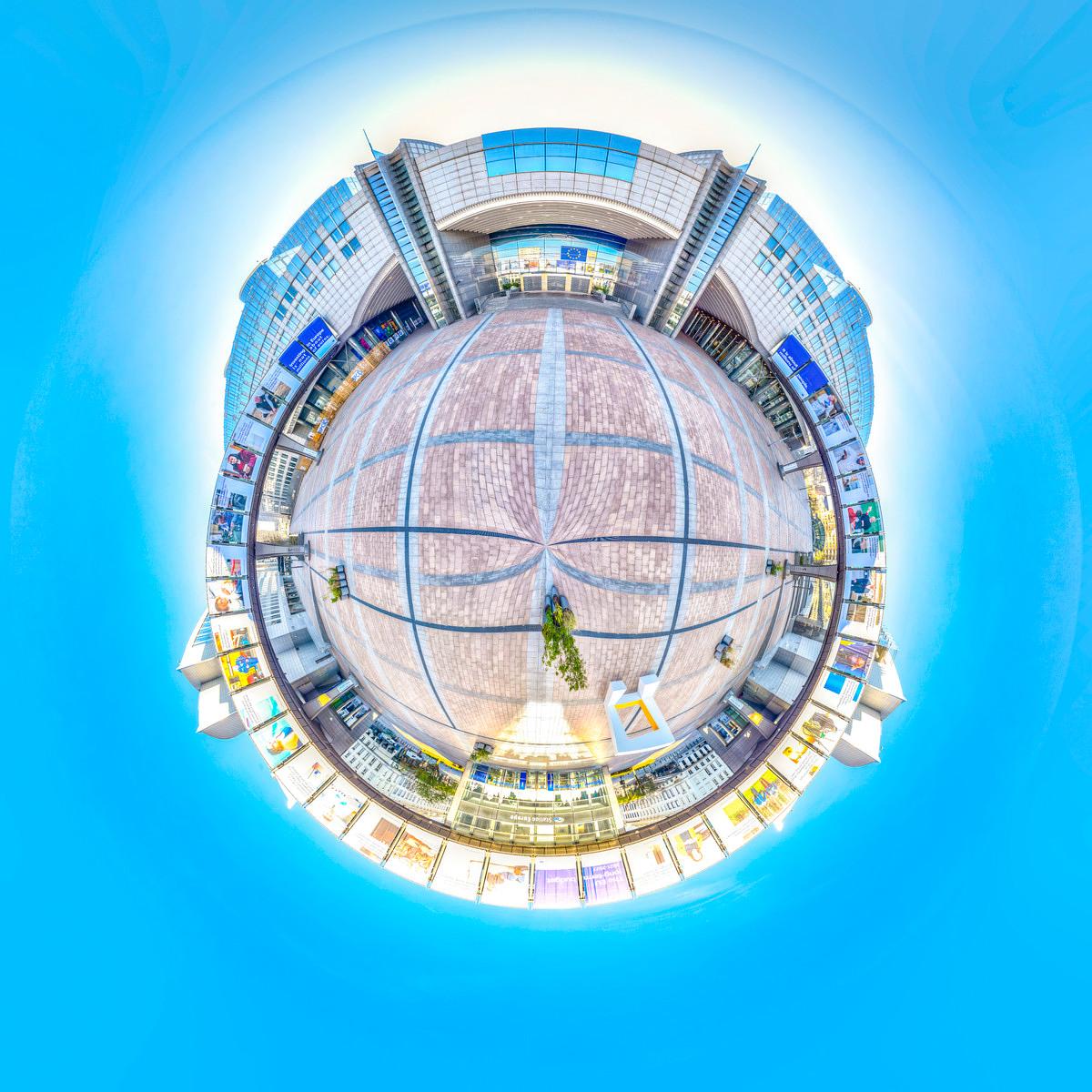 A 360-degree bird’s-eye view of the circular, cobbled forecourt, surrounded by modern glass-fronted buildings beneath a deep blue sky.