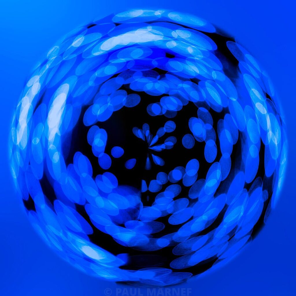 A blue spherical shape formed by luminous circular reflections swirling against a bright blue background, contrasting with a black central area.