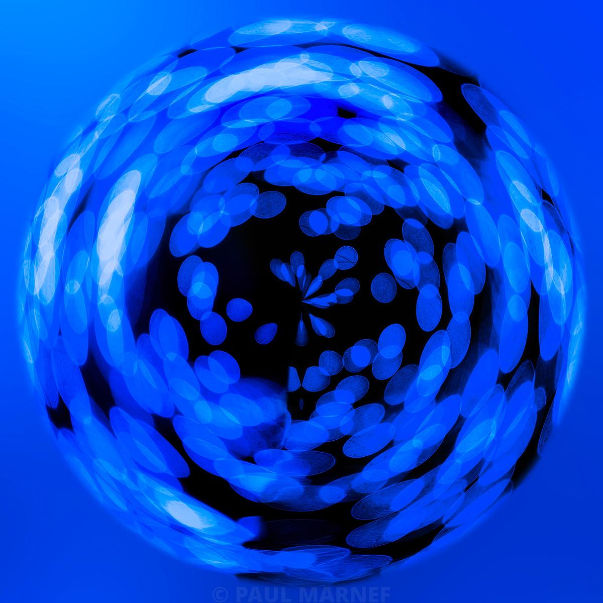 Forme sphérique bleue formée de reflets circulaires lumineux tournoyant sur un fond bleu vif, contrastant avec une zone centrale noire.