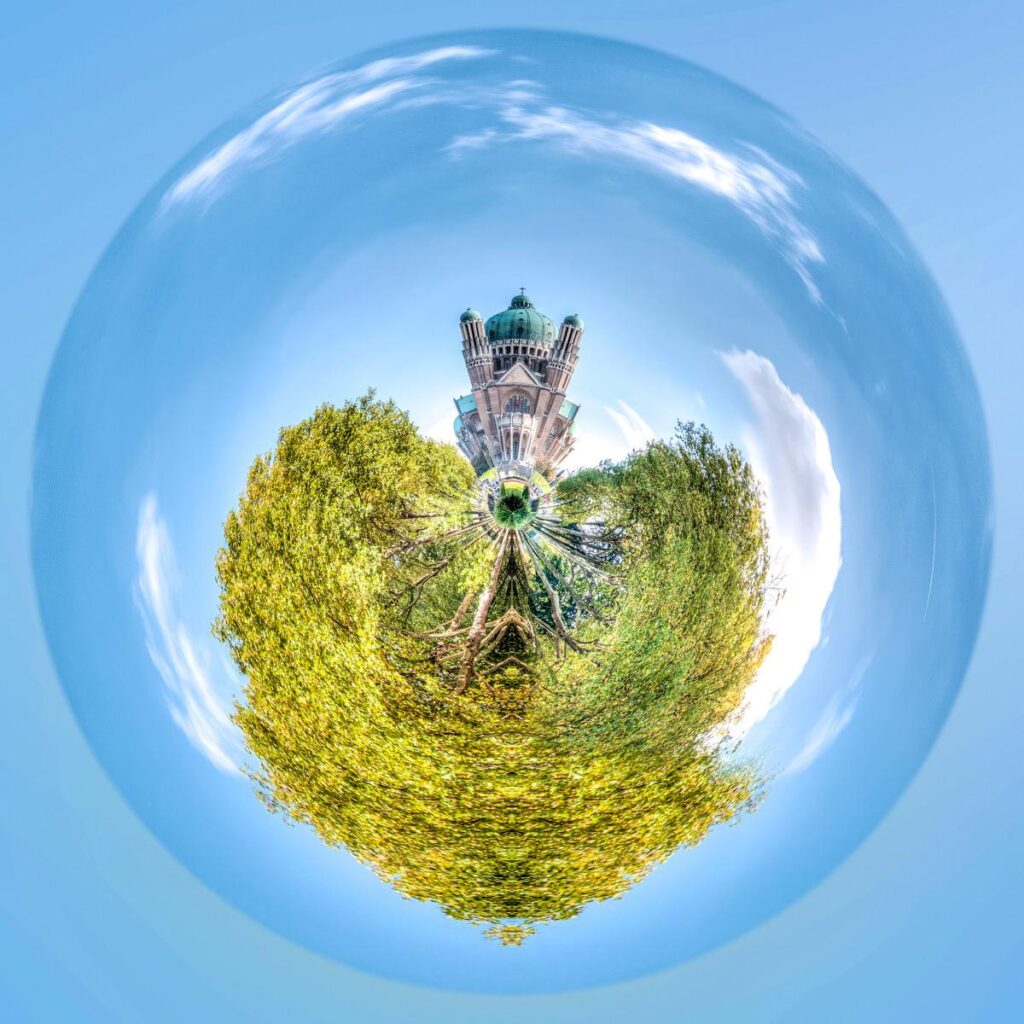 Une vue inversée d'une basilique à la flèche verte et de feuillages denses en forme de cœur cerclée par un vaste ciel bleu.