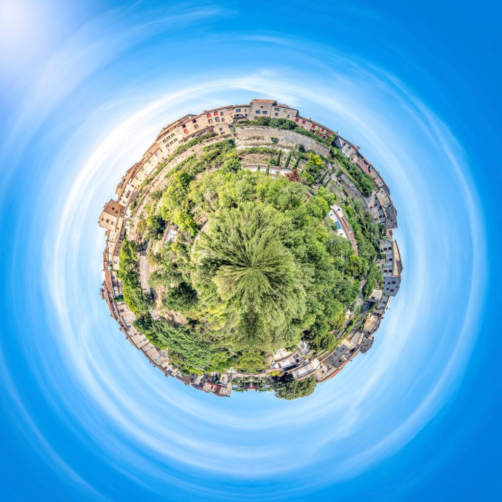 A stone village surrounded by dense vegetation and vineyards, standing alone against a clear, deep blue sky.