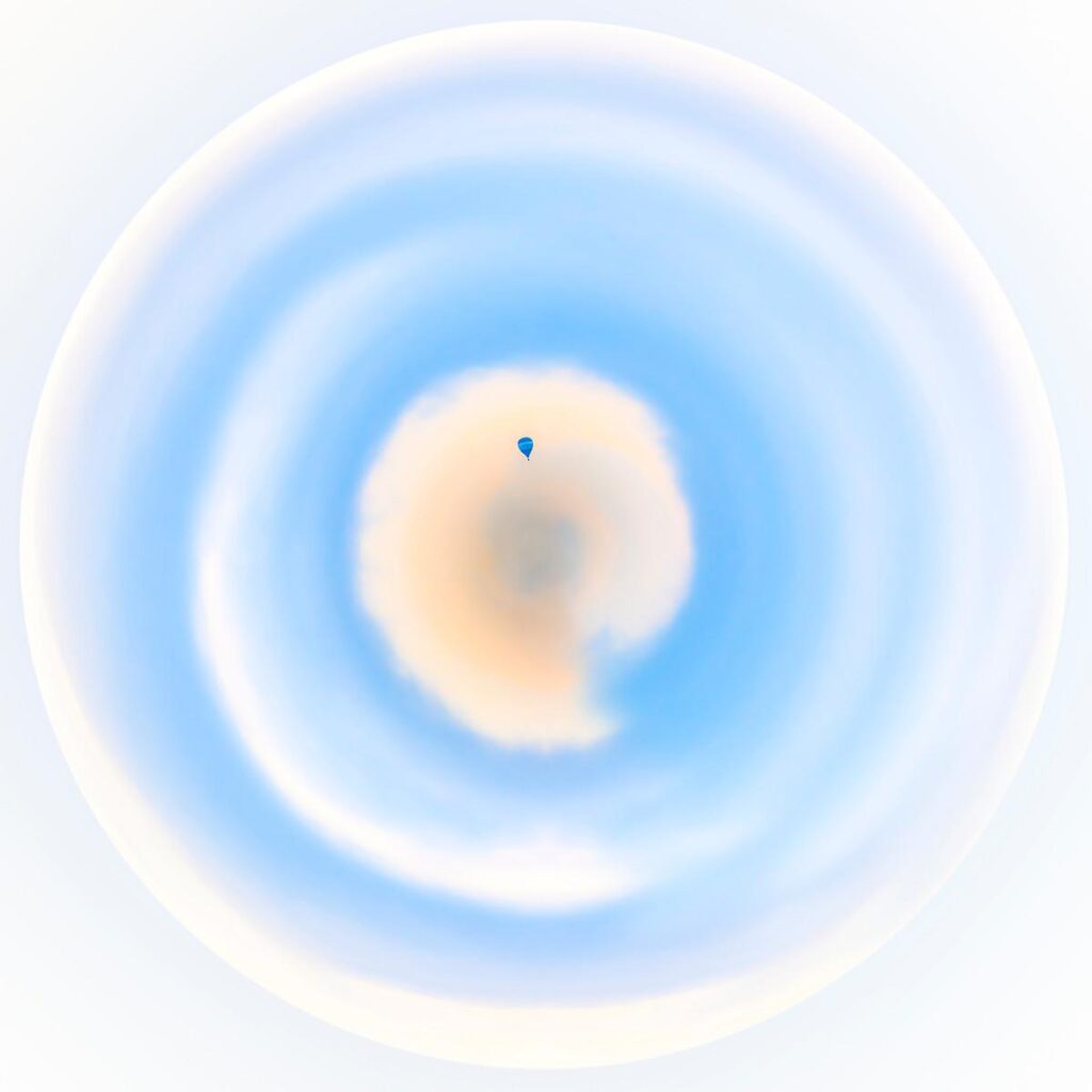 Vue plongeante d'une forme circulaire oscillant entre le bleu clair et le blanc, incluant une poche pâle au centre surmontée d'un point minuscule et bleu.