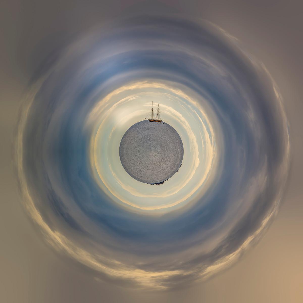 A circular, bluish, stormy veil enveloping a two-masted sailing ship on the grey sea, forming a central disc.