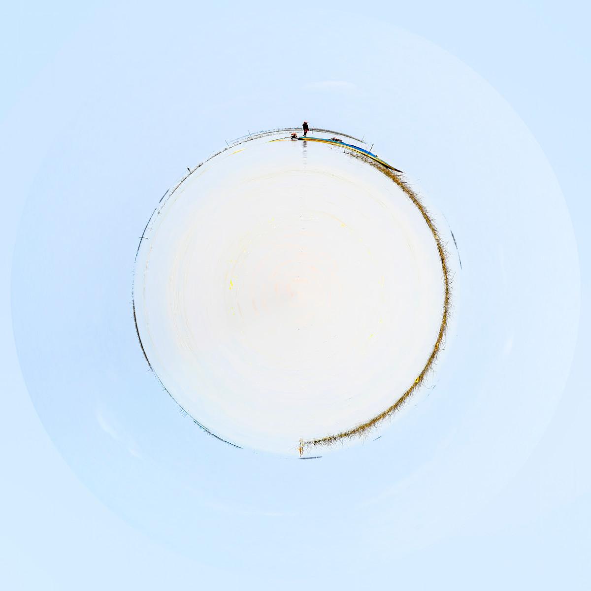 Cercle de neige immaculée avec un mince pinceau de végétation brune sur son pourtour et une silhouette solitaire au sommet contre le ciel.