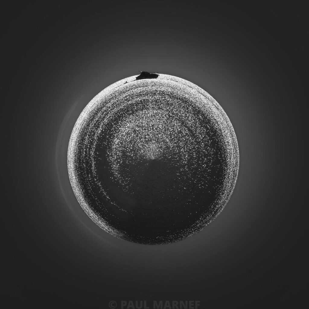 Un cercle texturé et granuleux au centre d'une surface sombre, délimité par une fine ligne brillante et incluant un fragment anguleux en haut.
