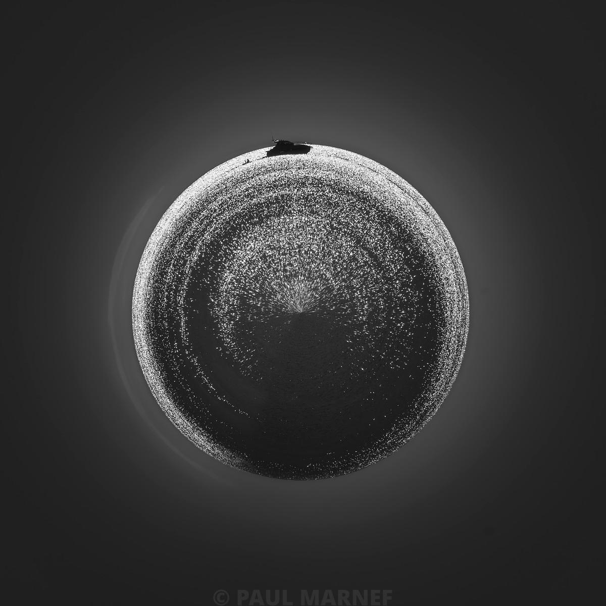 Un cercle texturé et granuleux au centre d'une surface sombre, délimité par une fine ligne brillante et incluant un fragment anguleux en haut.