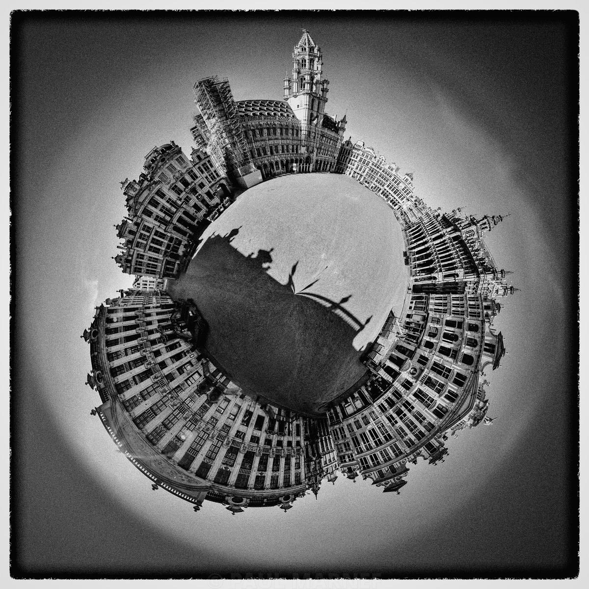 A black-and-white view of the Grand-Place, where the façades of the houses form a circular arc around a brightly lit square.