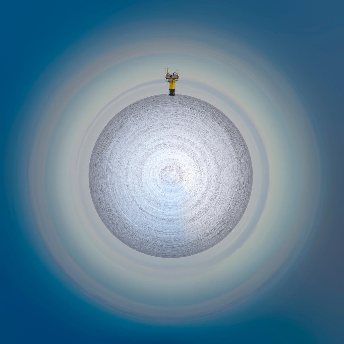 Une structure technique jaune couronne la pointe d'un globe de texture grise, encastré dans des cercles de ciel bleu pâle en dégradé.