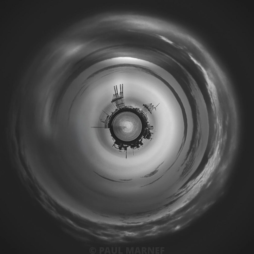 Tourbillon de nuages gris entourant une plateforme industrielle centrale par une vue trapézienne.