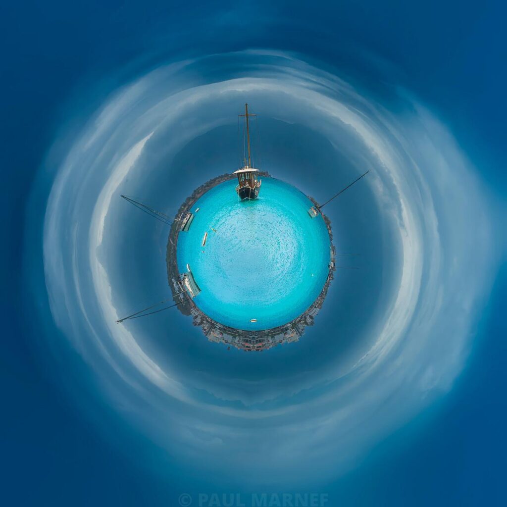 A turquoise bubble surrounded by clouds and a mast float in an ocean of blue mist.