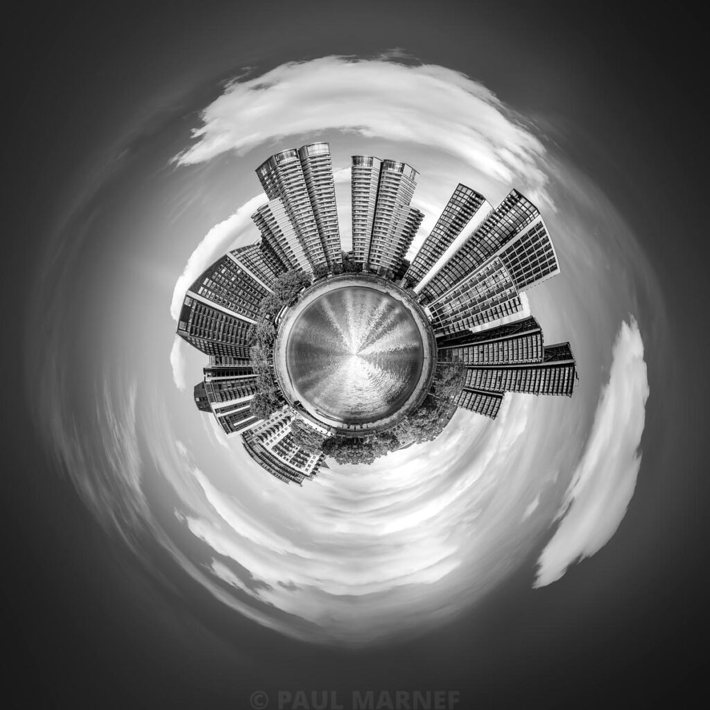 Street buskers arranged in a circle around a central fountain, with the sky swirling in a circular, fish-eye-style frame.