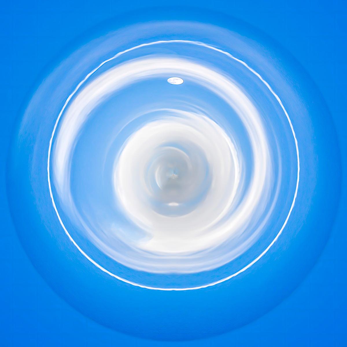 Un ciel bleu intense où des nuages blanc laiteux forment une spirale avec la lune pointue visible au-dessus des tours célestes.