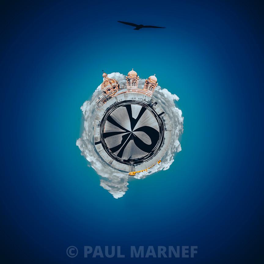 Une photo en poisson d'oeil où les toits de la Major forment un disque aérien entouré de nuages, sur une mer turquoise, alors qu'un oiseau survole.