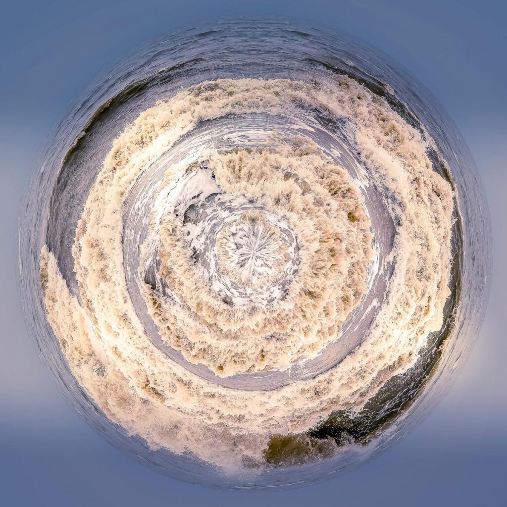 A 360-degree view of the maritime horizon across a vast expanse of ocean, with wave troughs filled with spray and swirling foam.