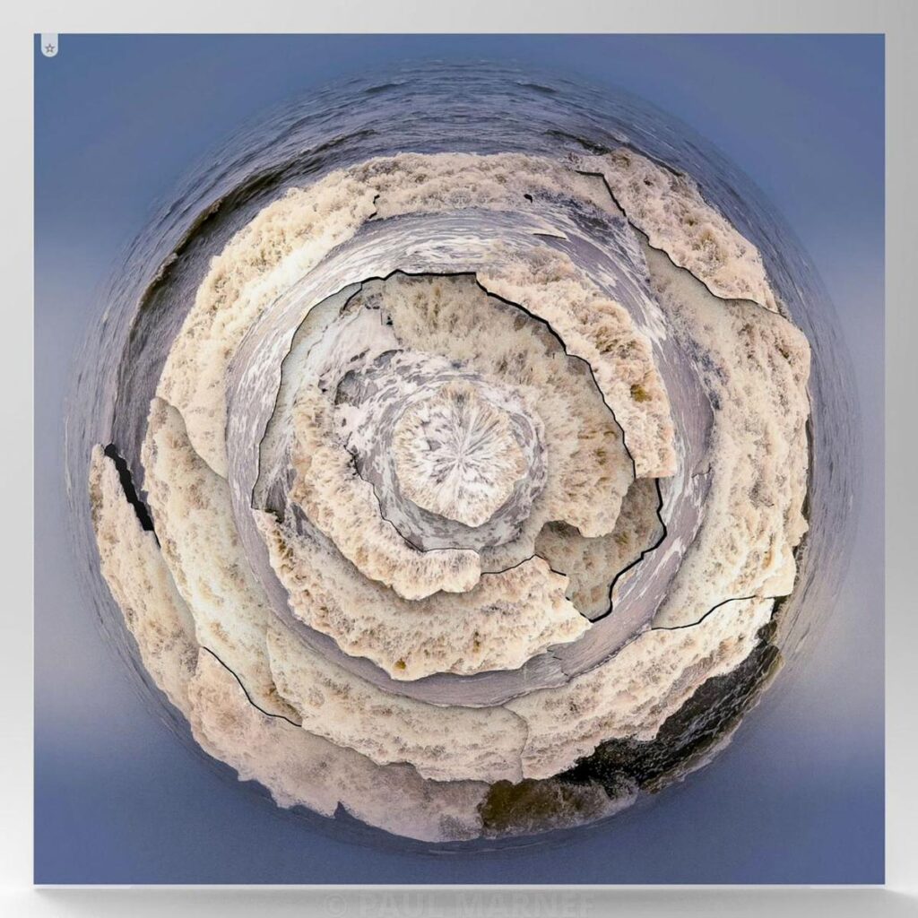 A spiral-shaped wave of white foam against a blue sea background.