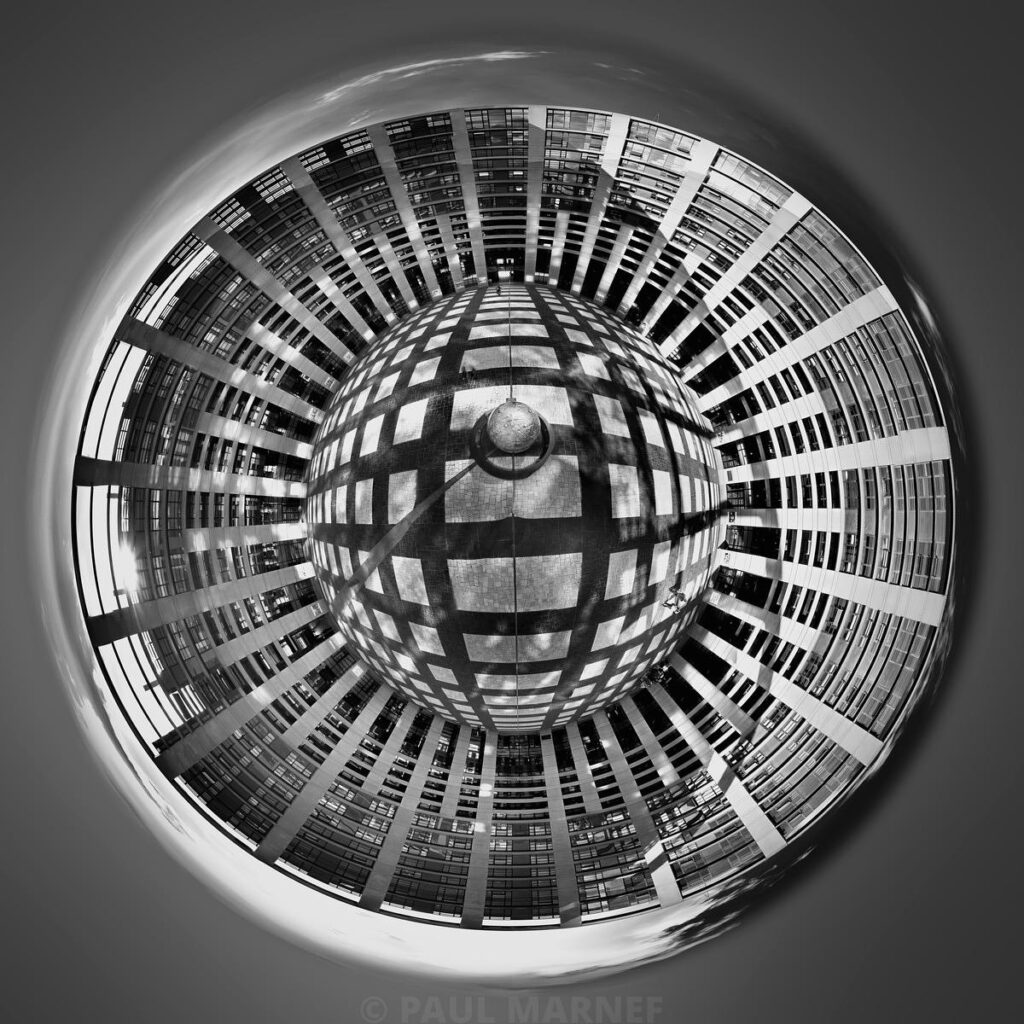 Sphère réfléchissante centrale dominant une façade de gratte-ciel aux reflets concentriques et géométriques en noir et blanc.