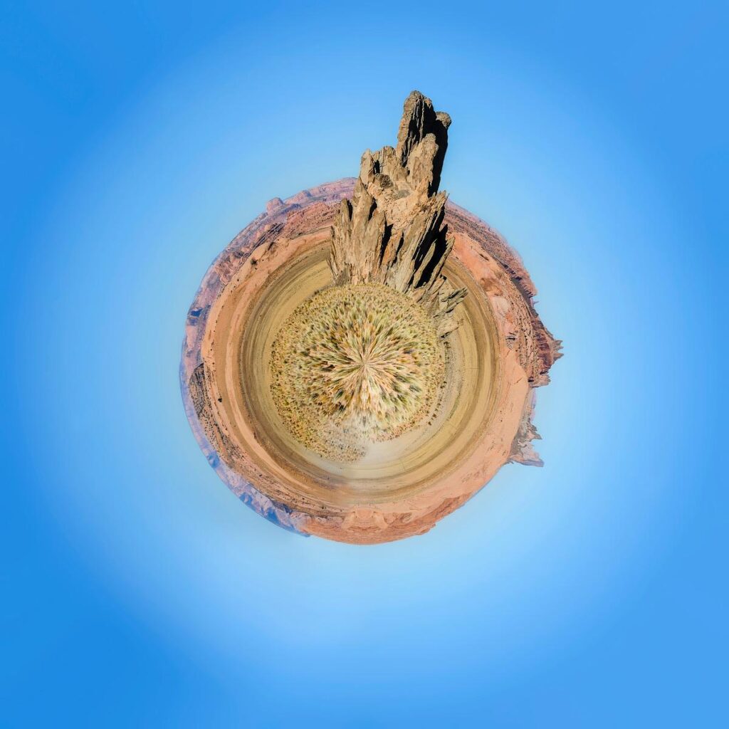 A 360-degree panoramic view showing a rock formation rising up in the centre of a rugged, arid landscape, set against a clear, deep blue sky.