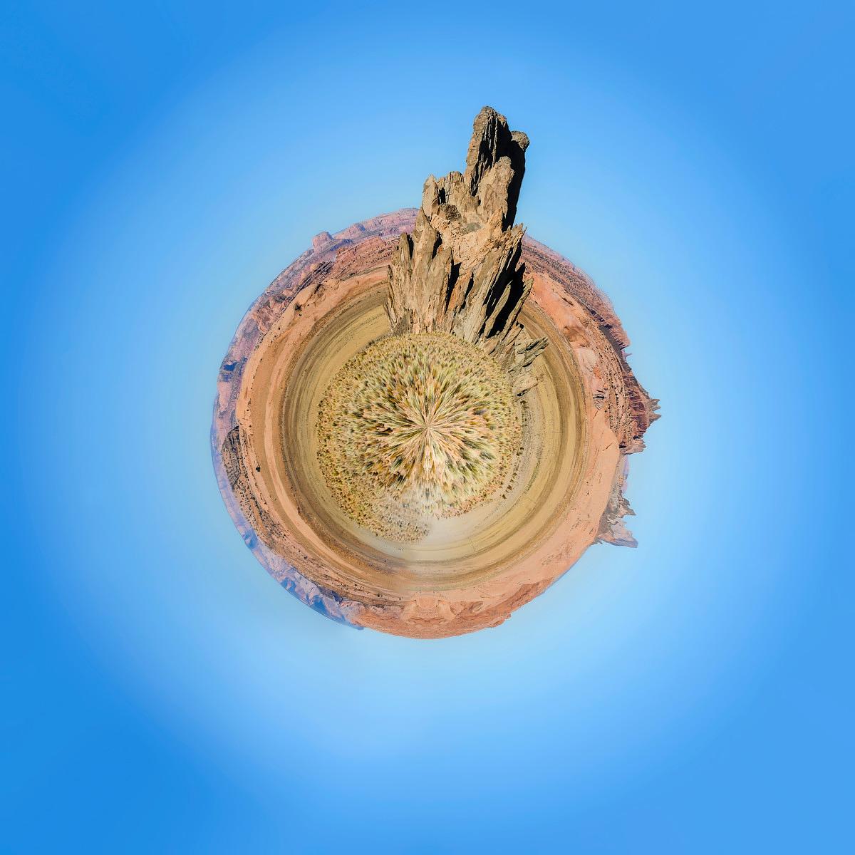 Vue panoramique 360 degrés où une formation rocheuse s'élève au centre d'un paysage aride déformé, encadré par un ciel bleu intense et dégagé.