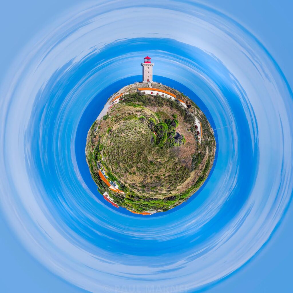 A white lighthouse with a red top on a lush, circular island surrounded by an azure blue ocean.