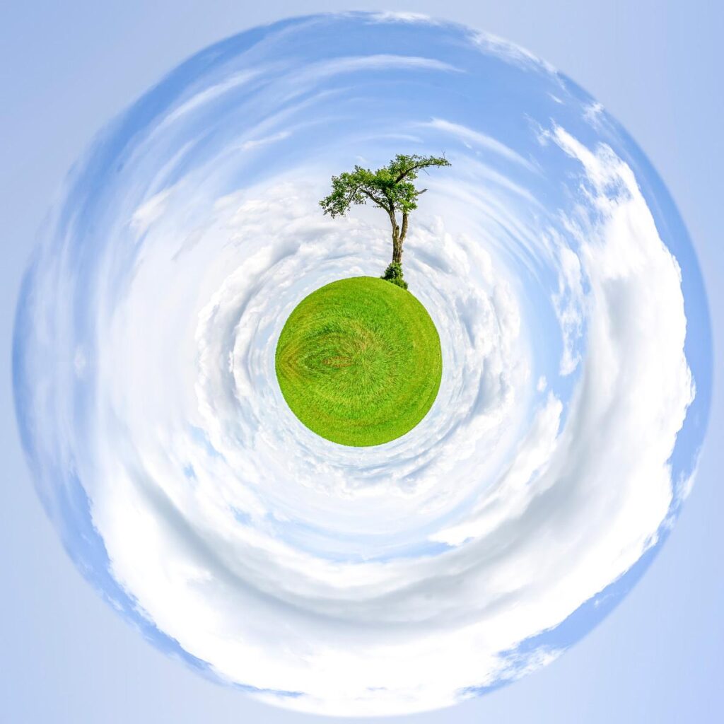 Un isolat d'herbe verte surmontée d'un arbre solo, enrobé de nuages blancs circulaires dans un ciel bleu.