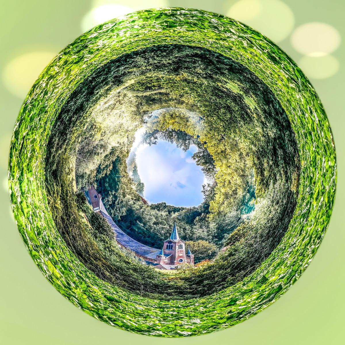 Vue sphérique d'un village avec une église à clochers, enclose par feuillages denses verticaux, ciel nuageux visible au creux du tunnel végétal.