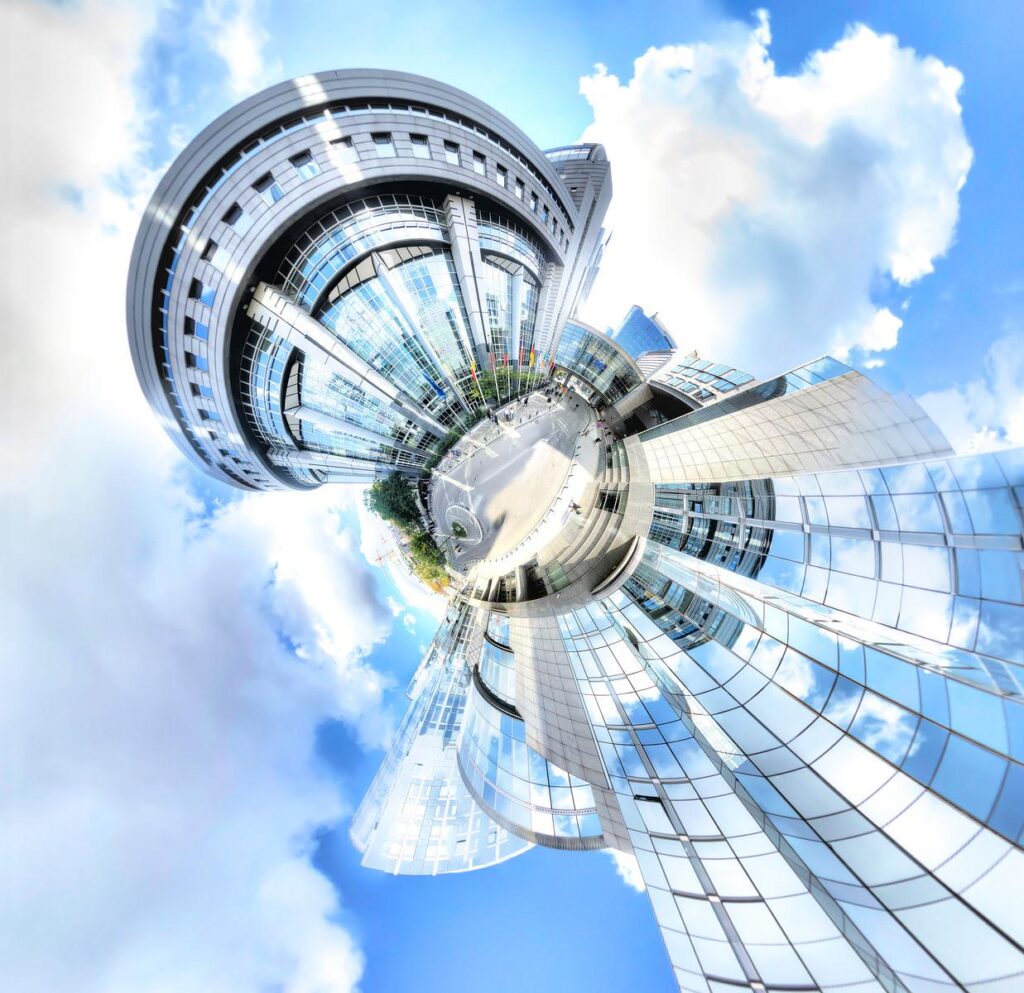 Vue en escalade d'un bâtiment courbe en verre se reflétant dans les nuages d'un ciel bleu.