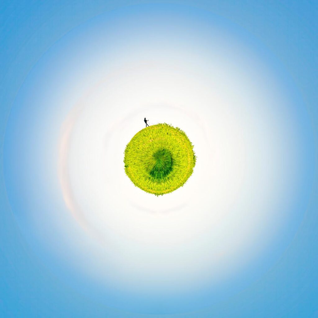 A green, globe-shaped blade of grass, isolated against a light background, with a tiny figure walking on it.