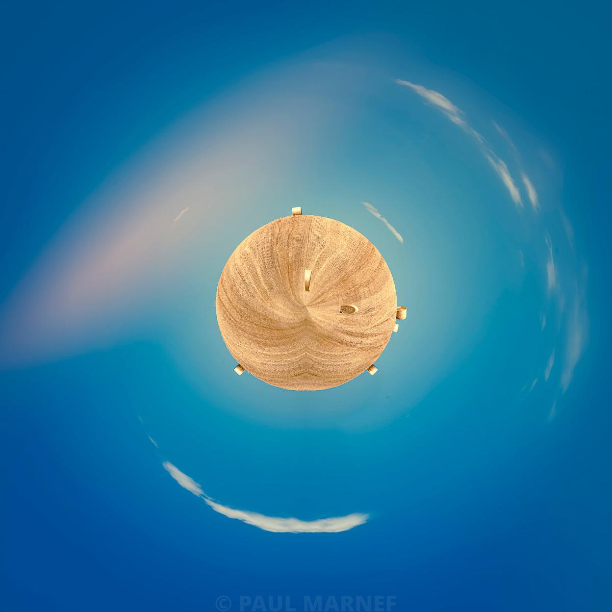 Un parasol en rotin centré, vu de dessus, sur un ciel bleu parsemé de fines traînées de nuages.