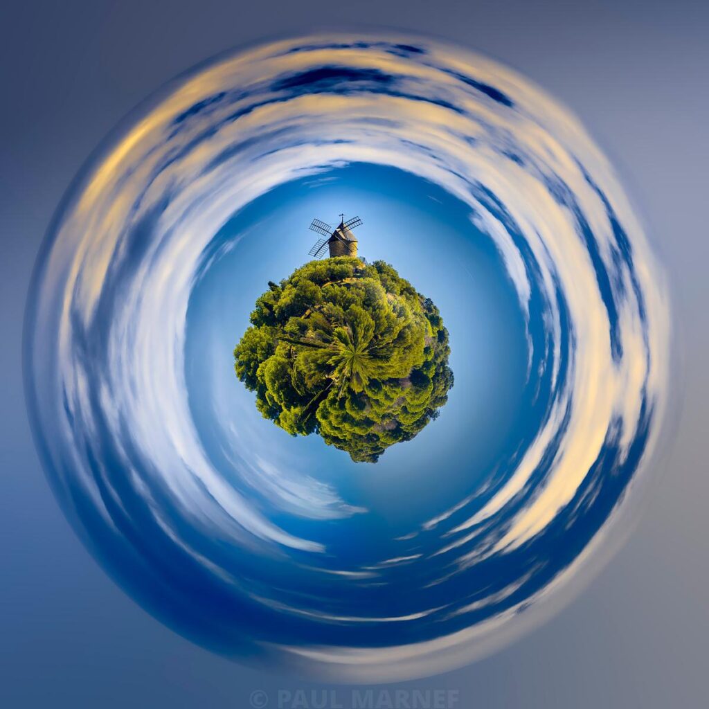 Éolienne sur une colline verdoyante entourée d'un ciel bleu avec des nuages circulaires créés par une longue exposition.