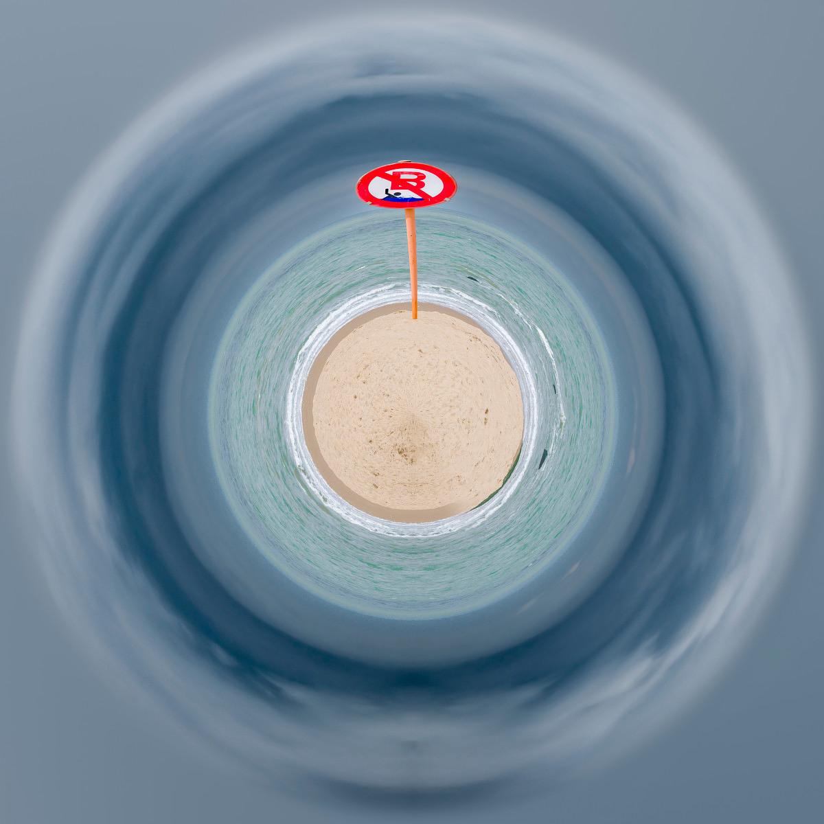 Vue plongeante sur une plage en forme de spirale où une vue floue forme des anneaux, un panneau rouge interdisant la baignade d'où part une ligne orange verticale.