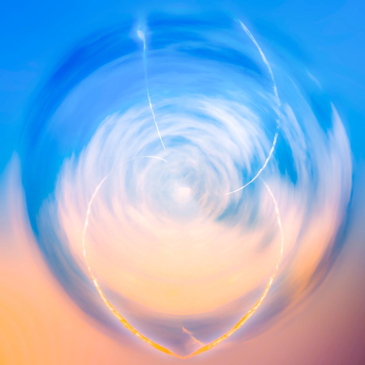 Flou rotatif vers un ciel bleu, un vortex nuageux et une traînée d'étincelles dorées sur un fond orangé pastel.