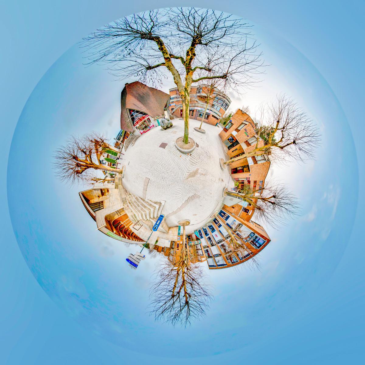 Vue 360 degrés de la Place Galilée, où un sol clair et un grand arbre dénudé entourent des immeubles aux façades de briques sous un ciel bleu.