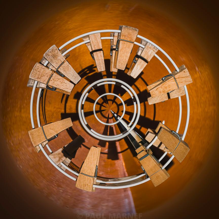 Pinces en bois écartées sur un socle circulaire blanc dessiné en spirale, projetant leurs ombres sur un fond chaleureux.