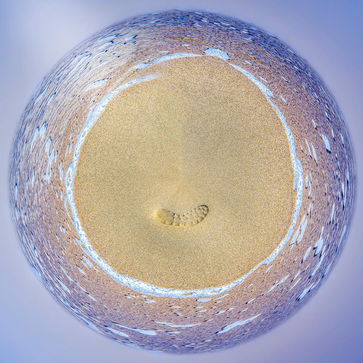Vue panoramique circulaire d'une plage avec une empreinte dans le sable entourée d'une vague d'écume sur une mer agitée.