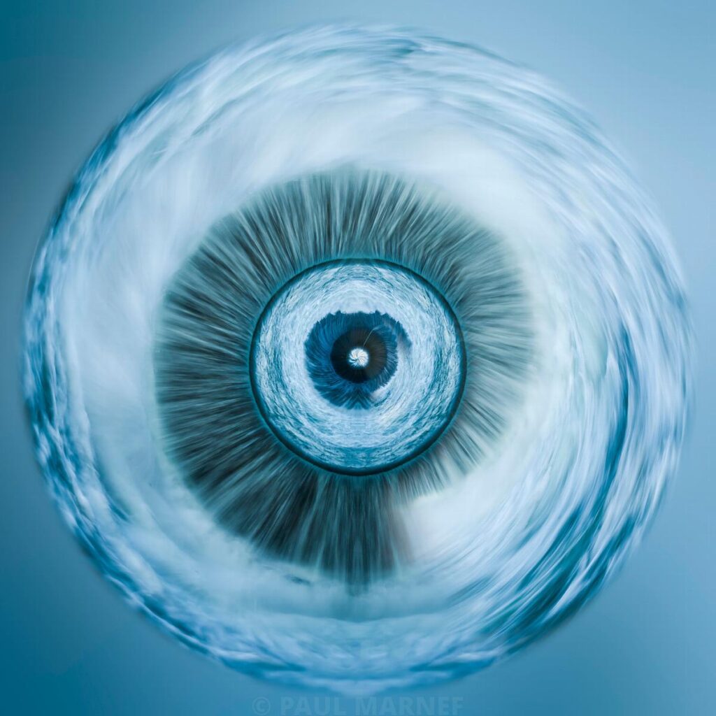 A close-up view of a human eye from the front, with moving water surrounding the milky-blue eyeball.