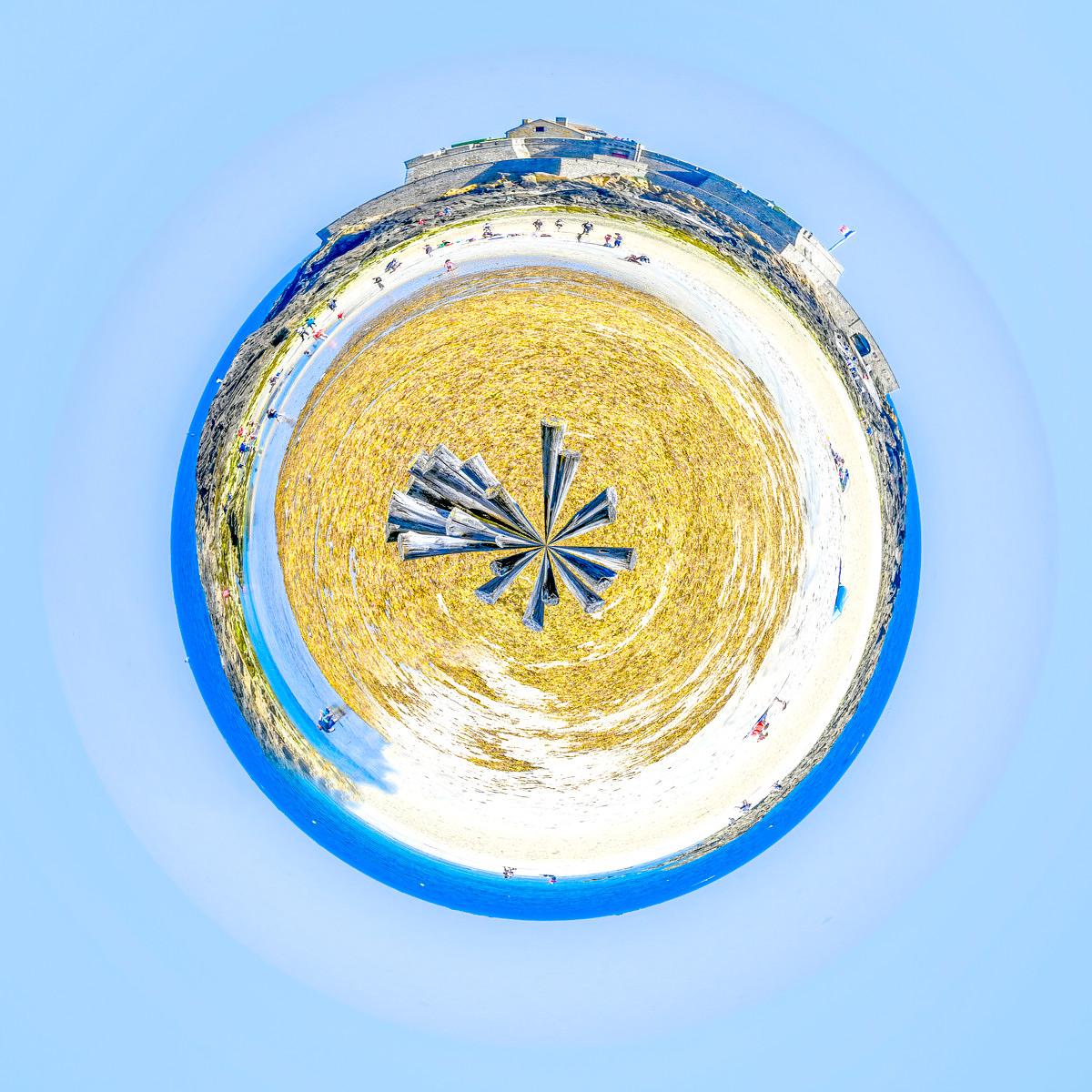 Planisphère 360 d'une plage sableuse avec parasols déployés, mont forterifié en arrière-plan, lagon turquoise et ciel bleu.