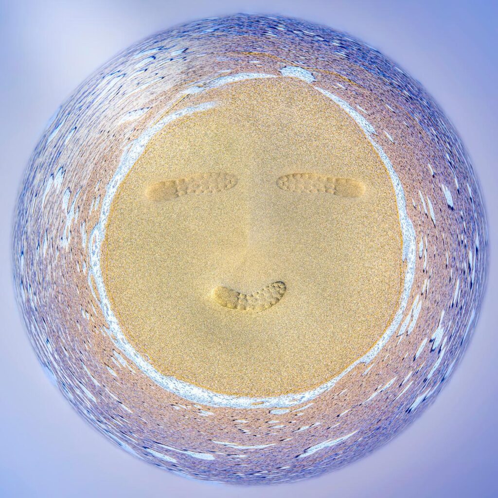 An aerial view transformed into a smiley face on a beach, showing boot prints in the sand.