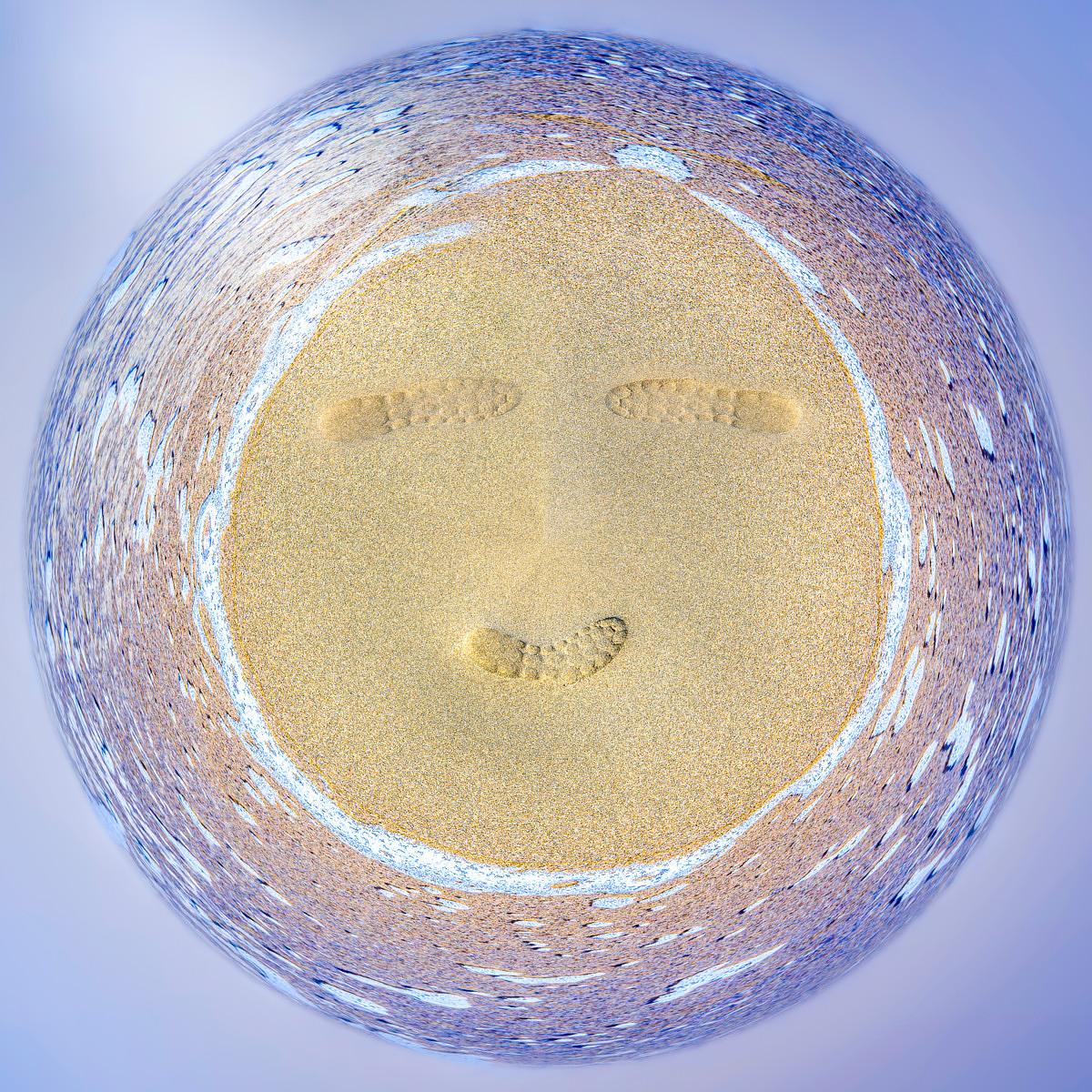Vue d'ensemble transformée en forme de smiley sur une plage, montrant des traces de pas de bottes dans le sable.