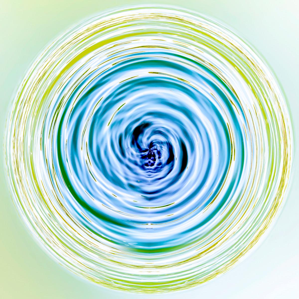 Un motif circulaire en spirale formé de tourbillons de liquide bleu, vert et jaune sur un fond clair.
