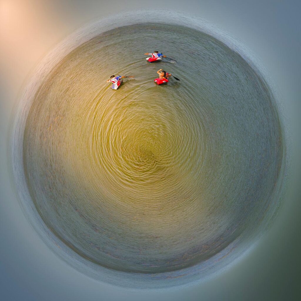 Vue aérienne en cercle où trois personnes en canoë jauni naviguent sur une étendue d'eau entourée de sable clair.