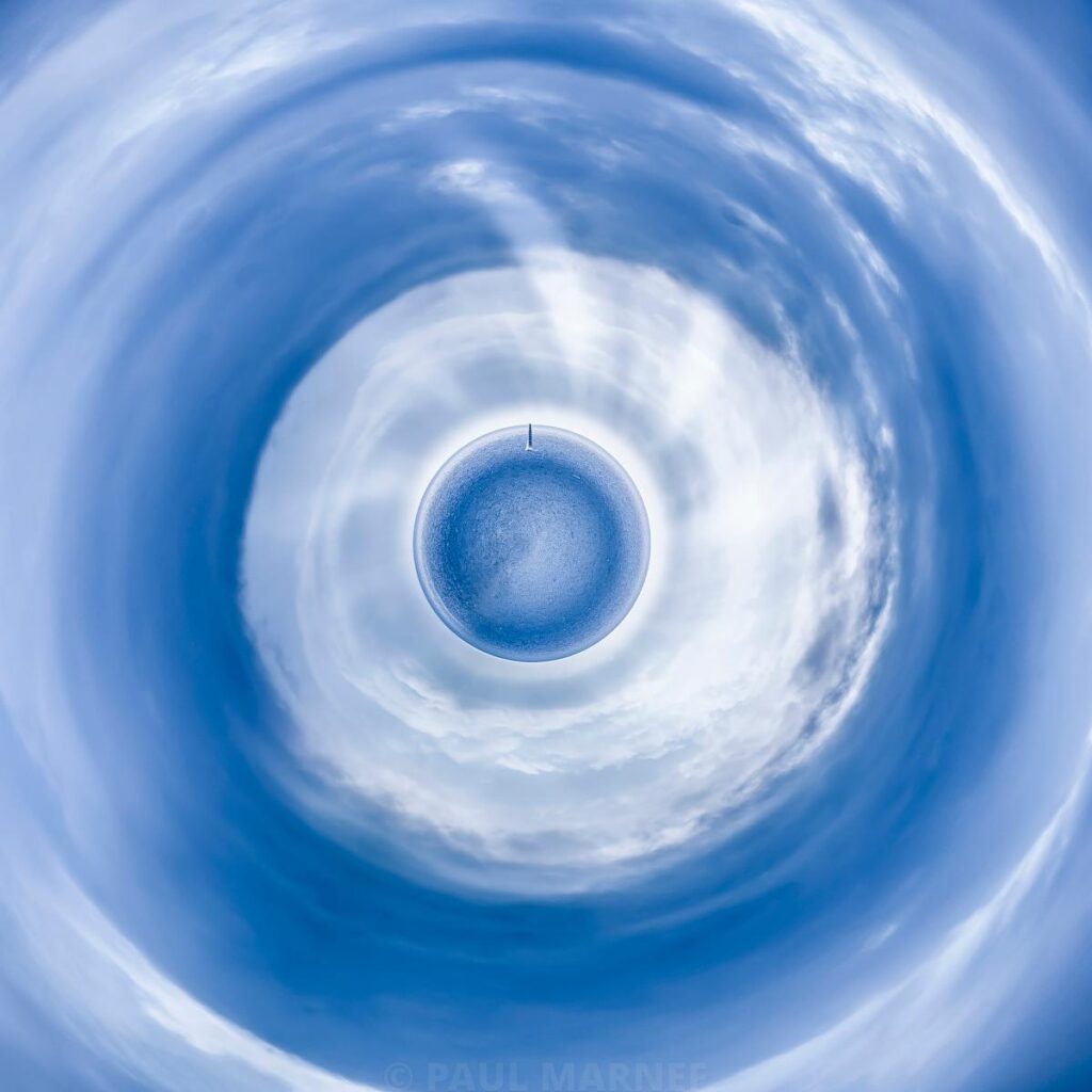 Sphère terrestre entourée d'un ciel bleu et de nuages blancs déformés en spirale, avec un ciel profond en arrière-plan.