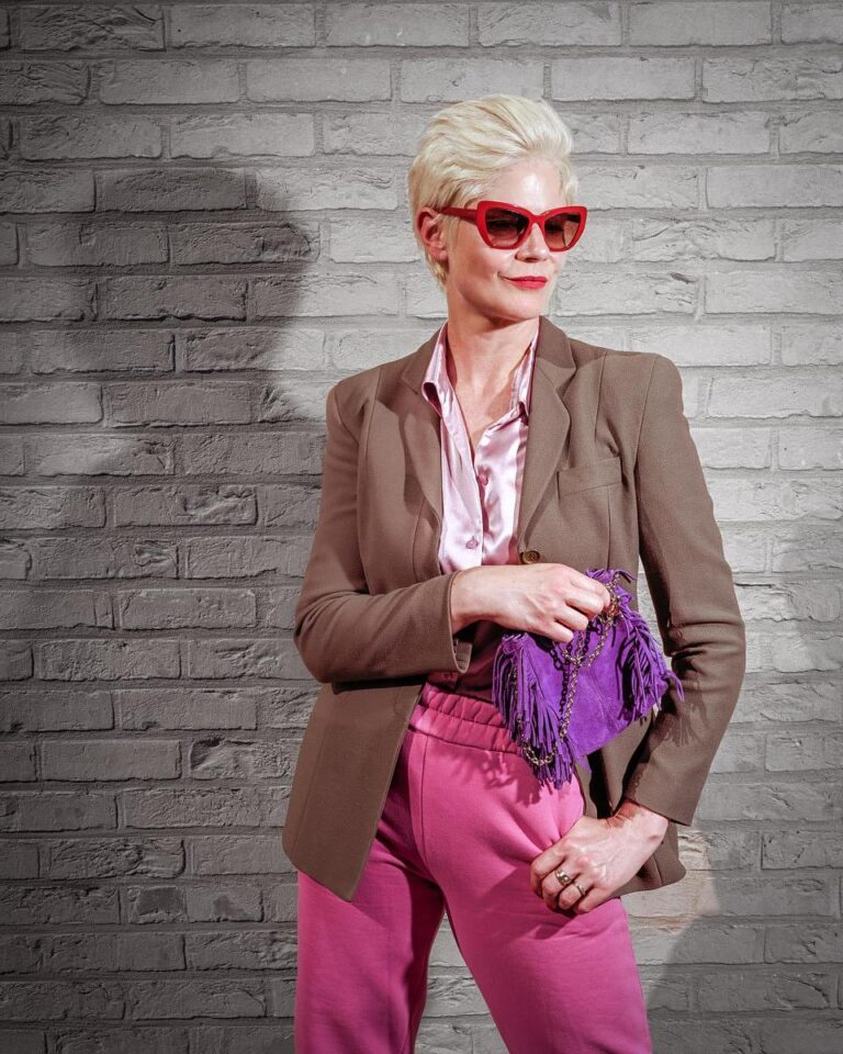 Portrait stylé d'une femme portant des lunettes rouges et un sac violet, capturé par Paul Marnef, photographe portraitiste à Bruxelles, avec un fond de briques créant un contraste moderne et audacieux.