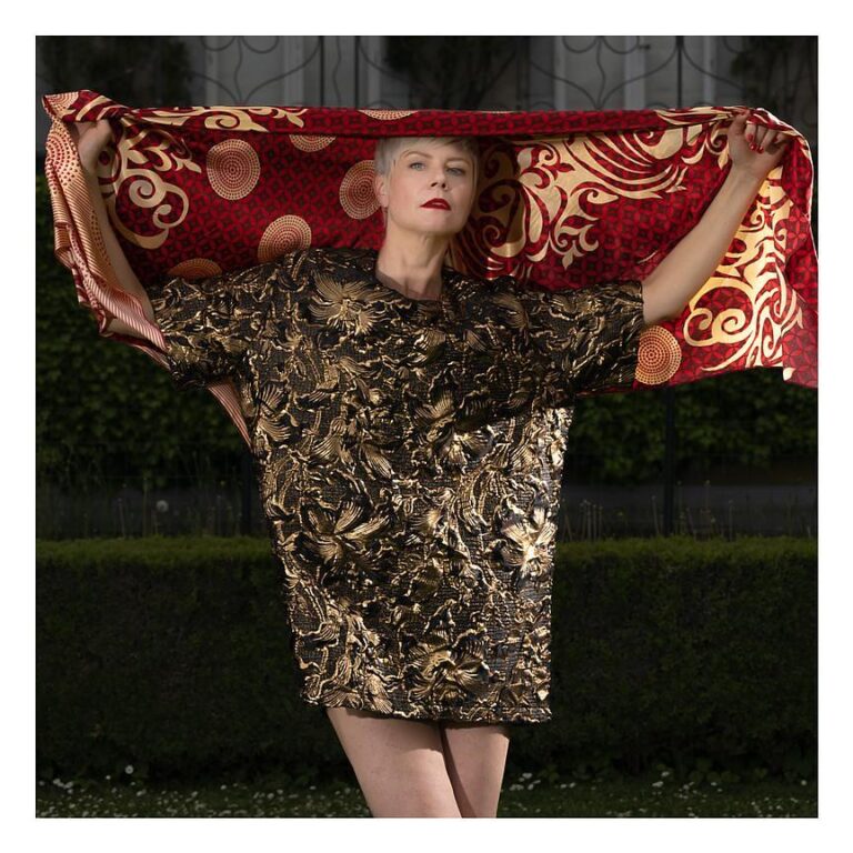 Portrait d'une femme élégante portant une tenue aux motifs dorés et un tissu rouge orné, capturé par Paul Marnef, photographe portraitiste à Bruxelles, révélant une forte présence artistique.