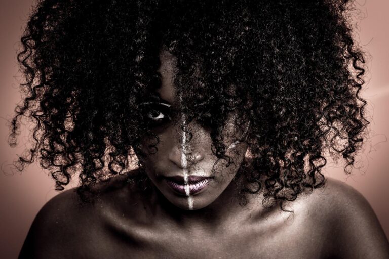 Portrait artistique d'une femme avec un maquillage tribal et une coiffure volumineuse, capturé par Paul Marnef, photographe portraitiste à Bruxelles, créant une ambiance mystérieuse et intense avec un jeu d'ombres.