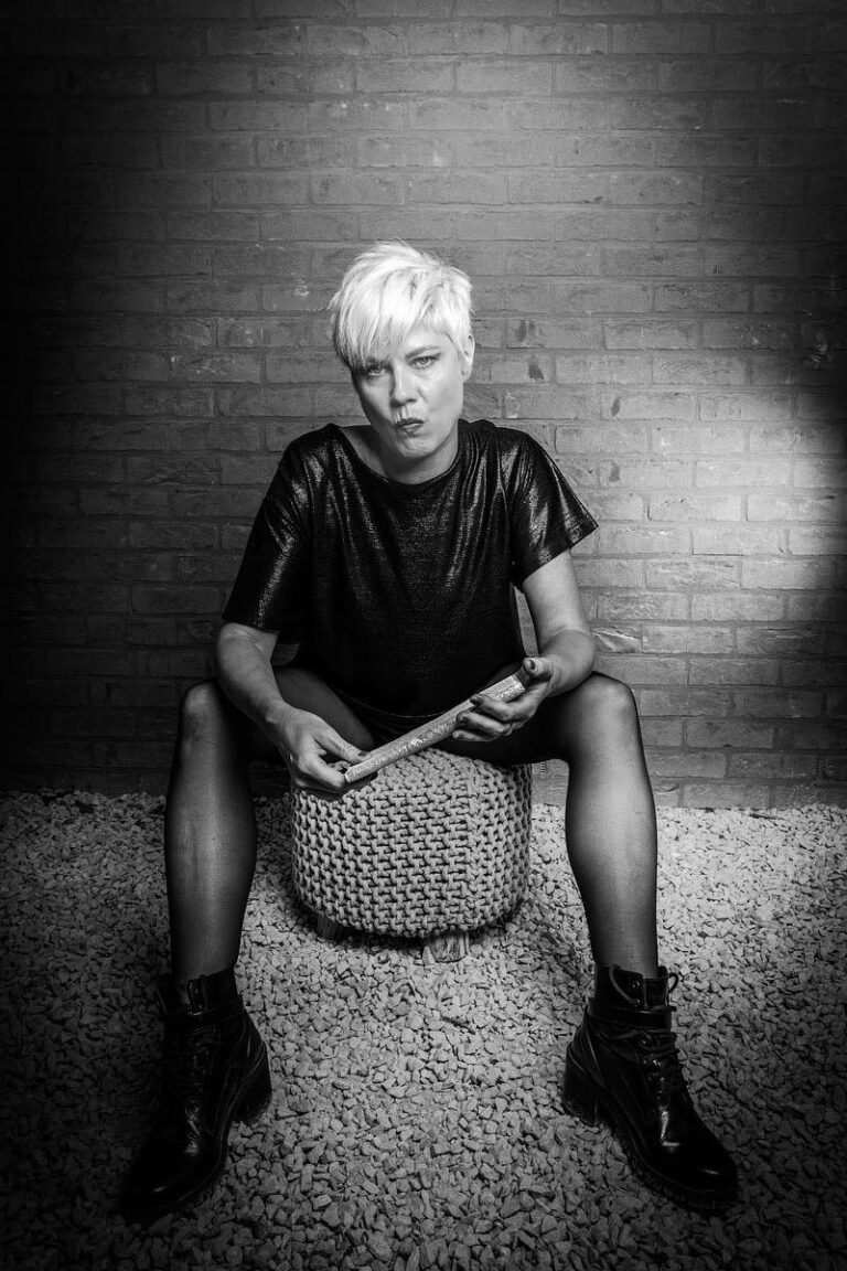 Portrait en noir et blanc d'une femme au style rock assise avec une posture affirmée, capturé par Paul Marnef, photographe portraitiste à Bruxelles, créant une ambiance brute et expressive.
