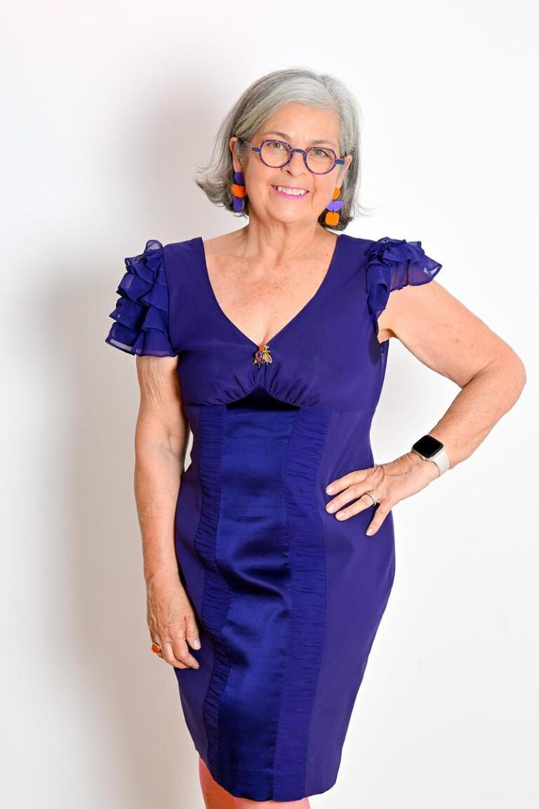 Portrait élégant d'une femme souriante en robe violette avec des accessoires colorés, capturé par Paul Marnef, photographe portraitiste à Bruxelles, exprimant confiance et style.